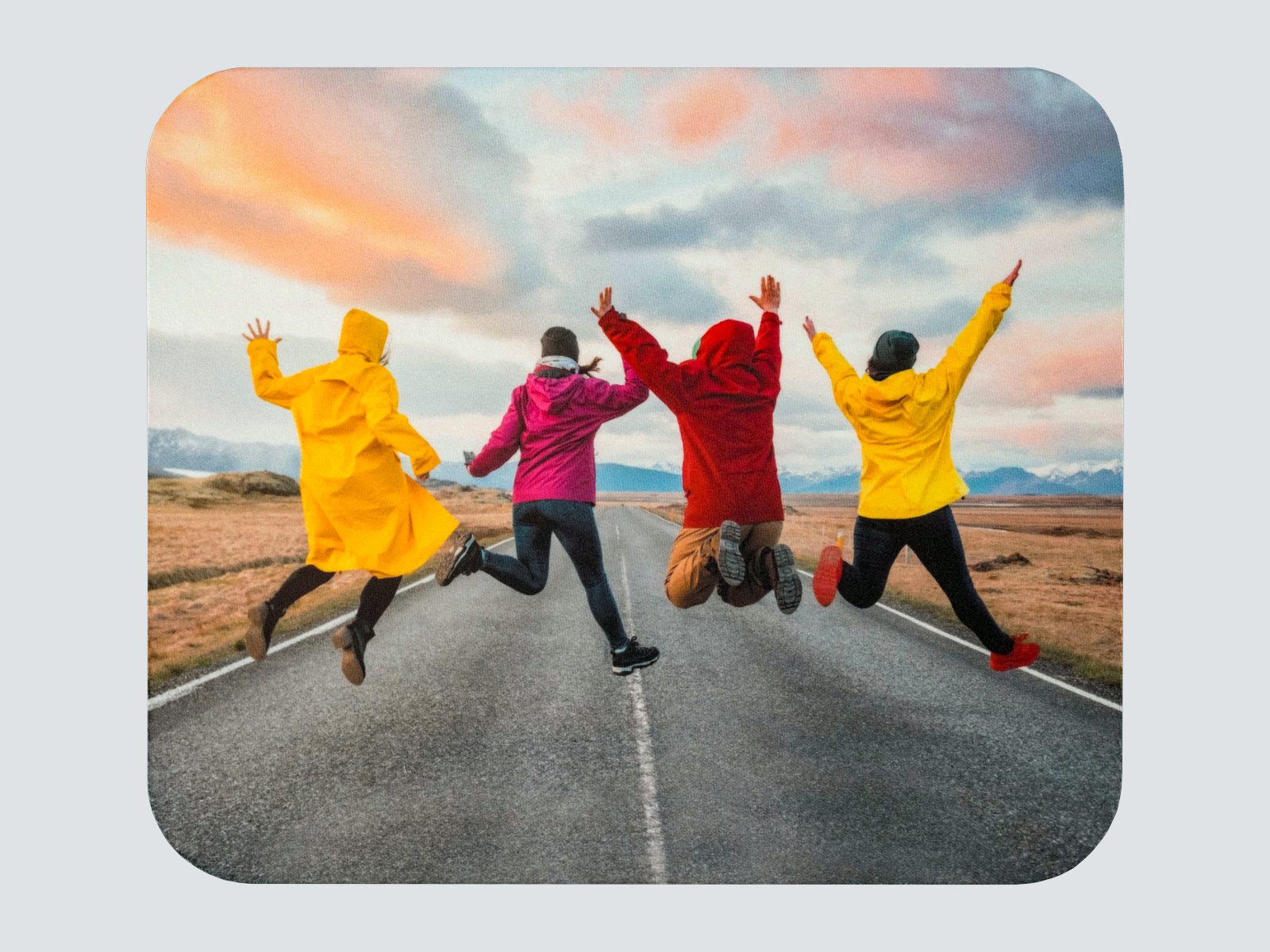 A rounded-corner mousepad with four friends jumping on an open road at sunset